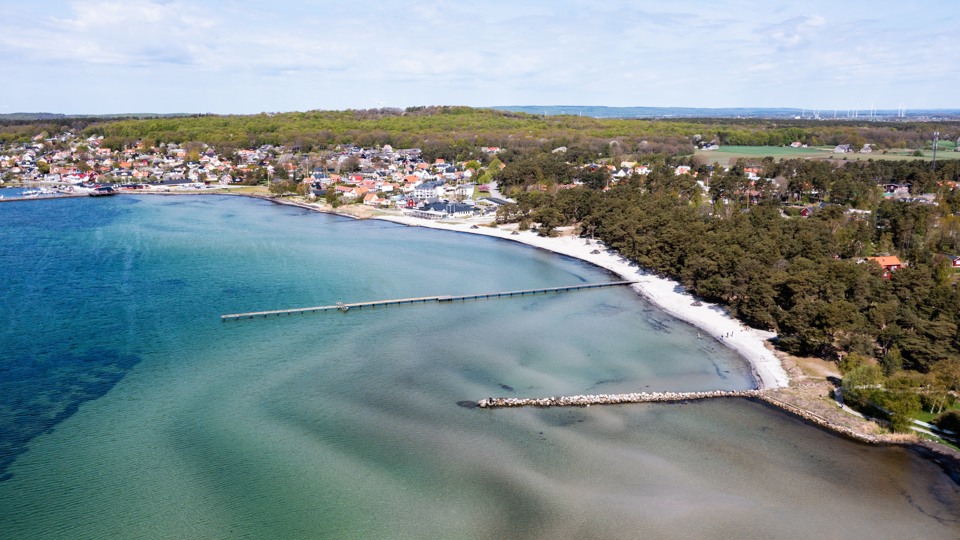 Flygfoto över kritvit sandstrand och Hälleviks pittoreska fiskeläge.