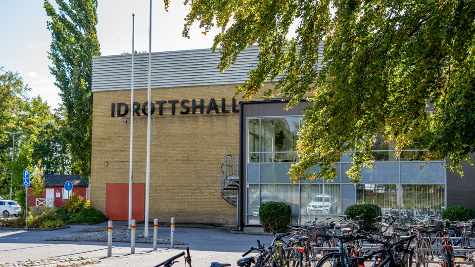 Bild på fasaden på Sölvesborgs idrottshall. PÅ gaveln på byggnaden står det idrottshall. Framför bågnanden finns träd och cyklar som står parkerade. 