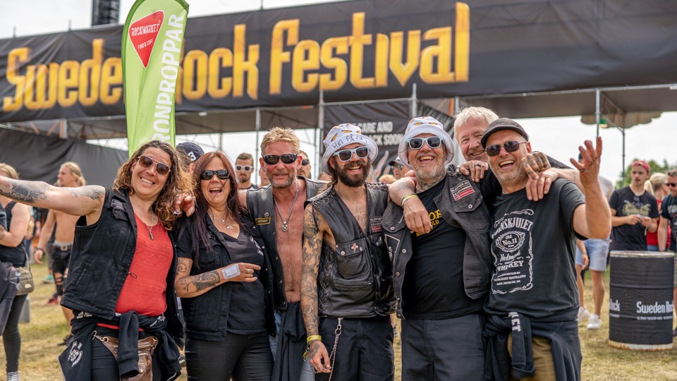 Ett glatt gäng i rockkläder står vid entrén till Sweden Rock Festival