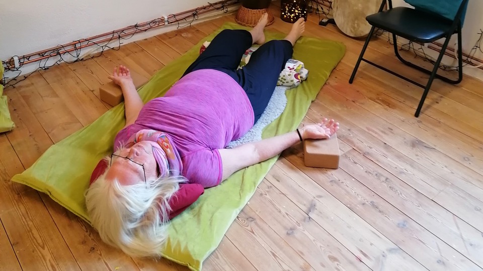 En kvinna ligger på en matta på golvet och gör en avslappningsövning.