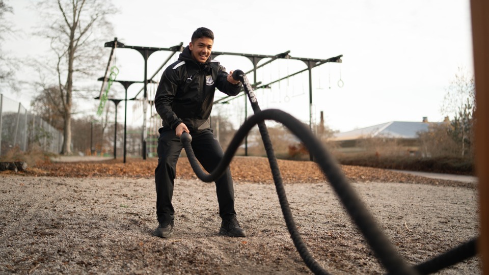 En kille står och håller i ett battleroe, ett tjockt rep som han slår upp och ner när han tränar.