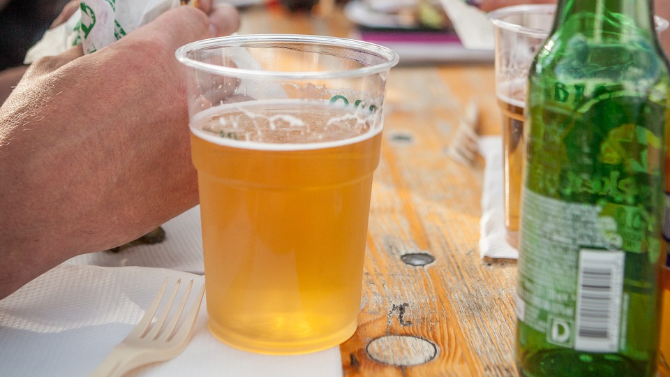 Ett plastglas med öl på ett bord bredvid en grön glasflaska