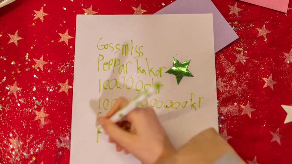 Ett barn skriver en önskelista, på den står det pepparkakor och 1 000 000 kronor.