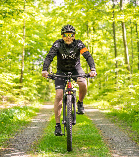 En man cyklar i bokskog på Ryssberget klädd i träningskläder