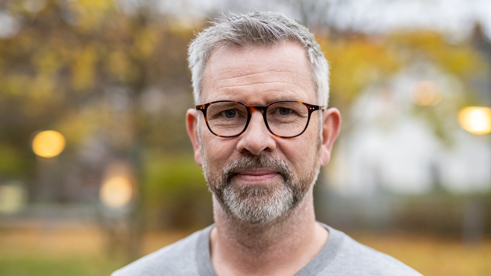 Bilden föreställer en man med glasögon, grått hår och gråsprängt skägg.