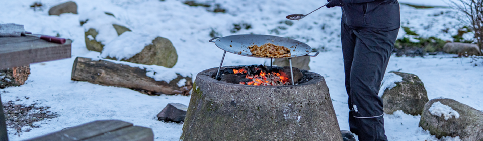 Kebabkött ligger på en murika som står över öppen eld mitt ute i ett snöigt vinterlandskap.