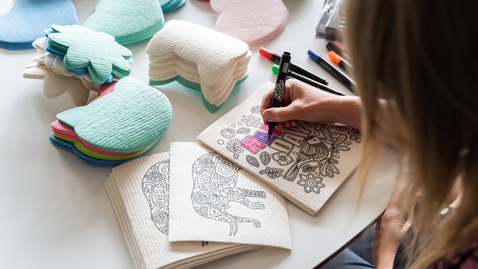En person färglägger ett mönster tryckt på en vit disktrasa.