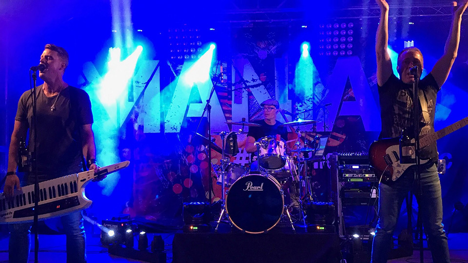 Tre bandmedlemmar i Maniac spelar och sjunger på en scen.
