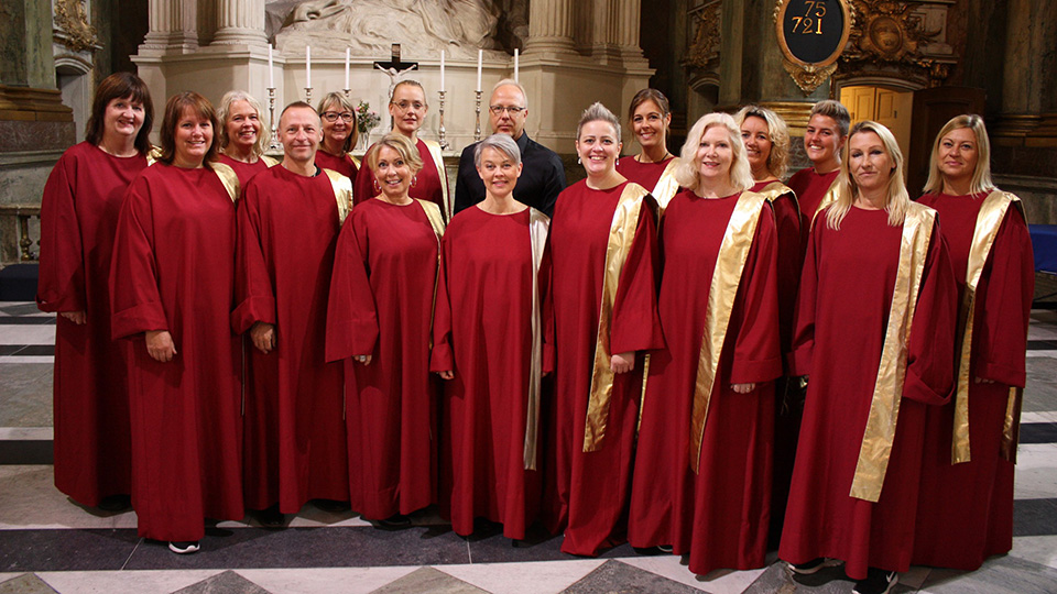 En gospelkör av kvinnor och män klädda i vackert röda dräkter stå i en kyrka.