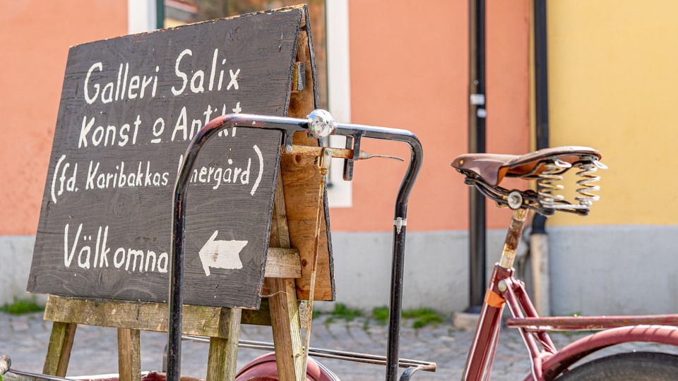 En gammal charmig cykel med en skylt som den står "Galleri Salix på" står på en kullerstensgata.