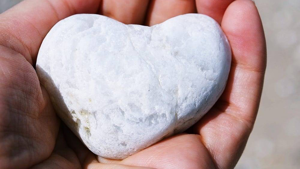 En person håller en sten formad som ett hjärta i sin hand.