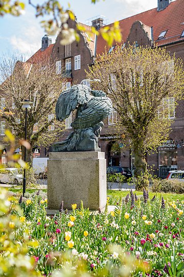 Staty står mitt i en blommande vårplantering i full blom.
